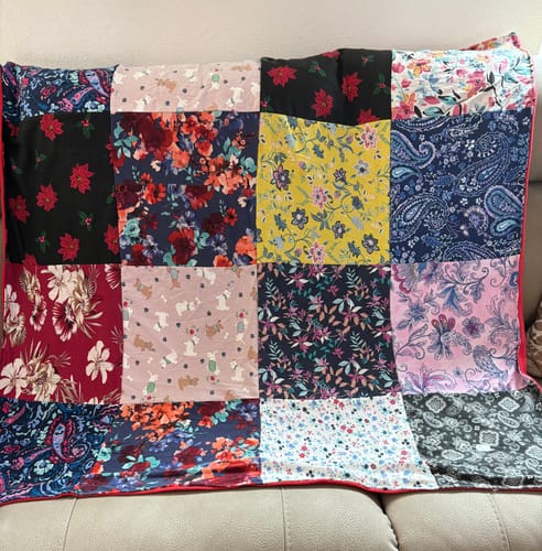 Customer's Project Repat T-Shirt Quilt, made with colorful patterned squares, laid across a couch.