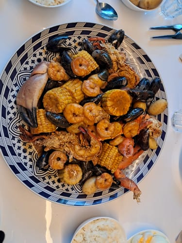 Klant toont een grote schaal met een heerlijke Cajun Seafood Boil, bereid met garnalen, mosselen en maïs.