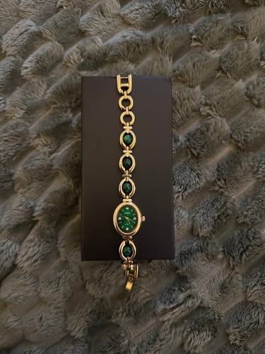 Customer's PERLE DE MAINS watch with green pearls and gold links, displayed on its box against a gray background.