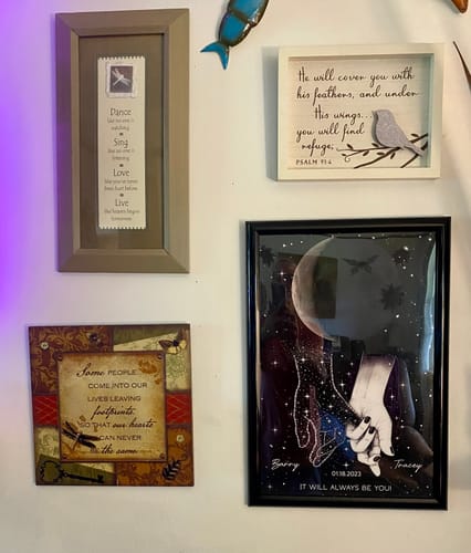 Reviewer's personalized memorial poster hanging on a wall with other framed art and memorial sayings.