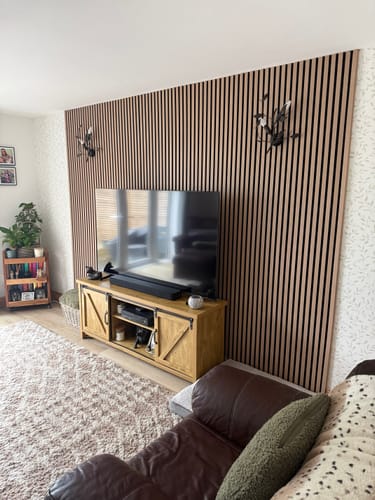 Customer's living room with Natural Oak acoustic wall panels installed behind a TV, creating a modern feature wall.