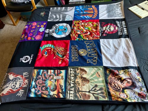 Customer's Project Repat T-Shirt Quilt with colorful, graphic panels from different t-shirts spread across a bed.