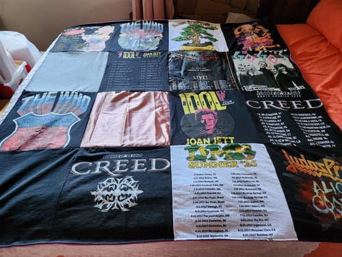 Customer's Project Repat T-Shirt Quilt made from various rock band t-shirts, including Creed and The Who, laid on a bed.