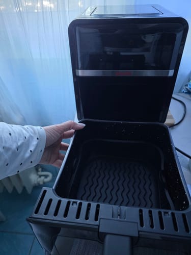 Client ținând în mână sertarul friteuzei Air Fryer Novio StonePro, arătând cuva adâncă cu tavă de silicon.