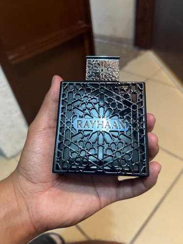 Un cliente sostiene en la mano el frasco negro del perfume Rayhaan Obsidian, que tiene un intrincado diseño geométrico.