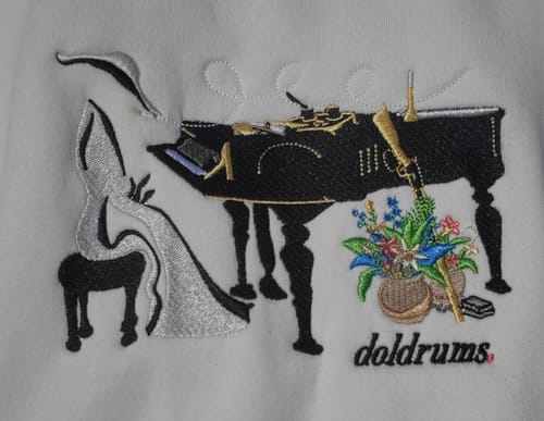 Close-up of a customer's custom crewneck showing intricate embroidery of a piano, a rifle, and flowers with 'doldrums' below.