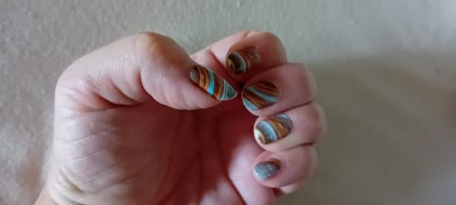 Kundin zeigt ihre Hand mit den bunten, gestreiften 'Metallic Marble' Nagelfolien.