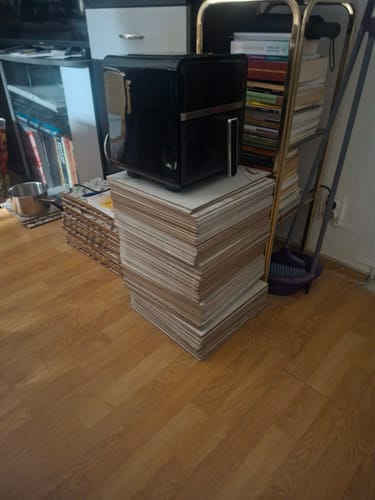 Friteuza neagră Air Fryer Novio StonePro a unui client, așezată pe un teanc de obiecte într-o cameră.