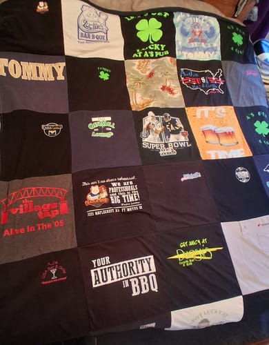 Partial view of a customer's Project Repat T-Shirt Quilt, showing various custom shirt squares laid on a bed.