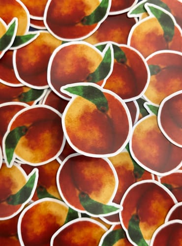 Reviewer's pile of custom vinyl stickers featuring a vibrant peach design with a white border.