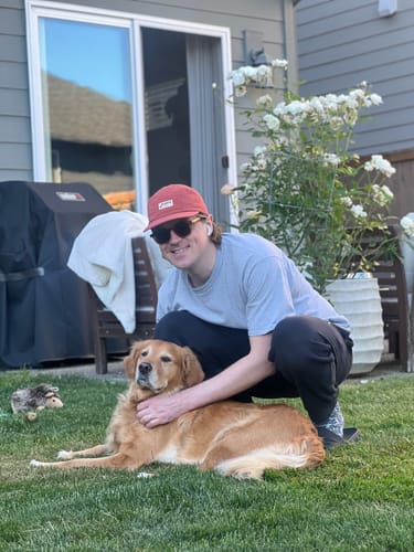 Customer wearing the red Big Camp Hat while smiling and petting a dog outdoors.