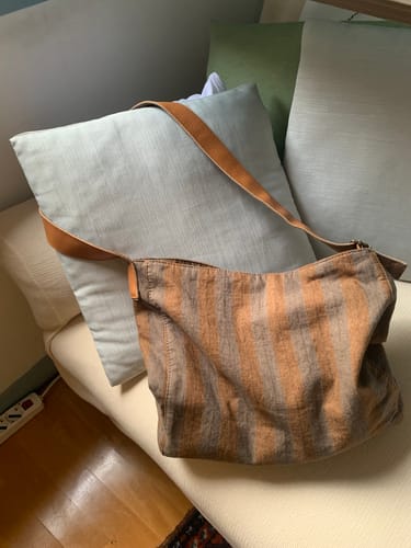 Customer's striped canvas bag with a brown strap resting against a pillow on a couch.