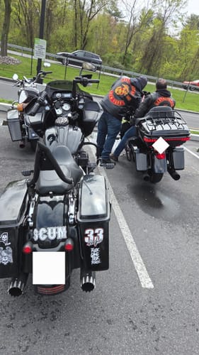 Customer's LARGE SCUM STICKER on the backrest of a black motorcycle in a parking lot with another person nearby.