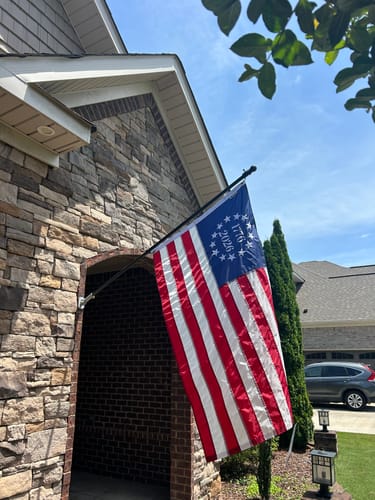 Customer's 1776 to 2026 Betsy Ross Flag flying from a flagpole on the front of a brick and stone house.