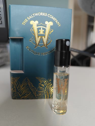 Customer's sample vial of Copacabana perfume standing next to its decorative teal and gold box on a desk.