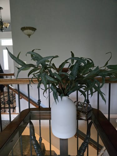 Reviewer's Faux Willow Eucalyptus stems displayed in a modern white vase on a table by a staircase.