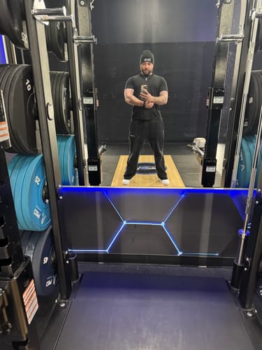 Reviewer taking a mirror selfie in a gym, wearing black Classic Baggy Sweats and a beanie.