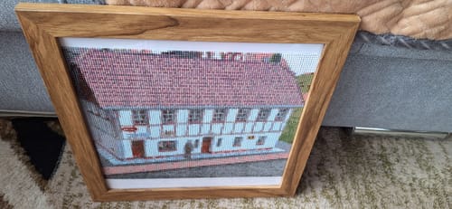 Rezensent zeigt das gerahmte, fertige Diamond Painting eines Fachwerkhauses.