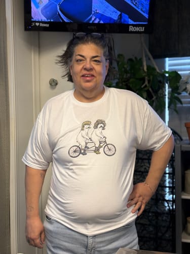 Reviewer standing indoors wearing the white Bike Polar t-shirt with a graphic of two polar bears on a tandem bicycle.
