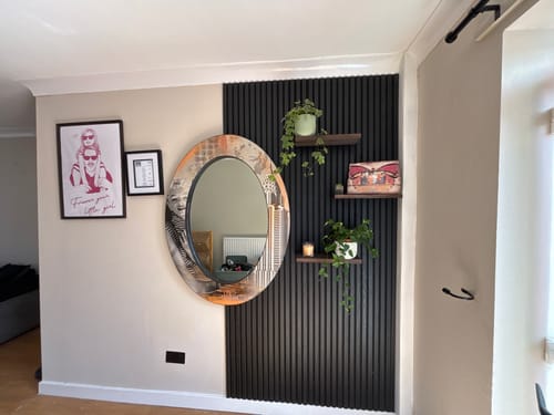 Customer's black Premium Acoustic Wall Panels installed as a feature wall, decorated with shelves and an oval mirror.