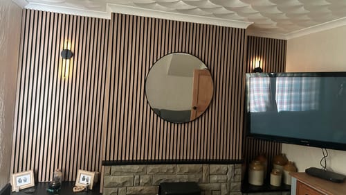 Customer's living room with Natural Oak acoustic wall panels installed on a feature wall above a stone fireplace.