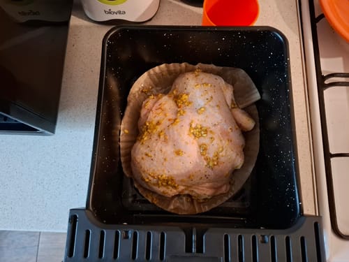 Recenzent arată un pui crud, asezonat, în cuva antiaderentă a air fryer-ului Novio StonePro, înainte de gătire.