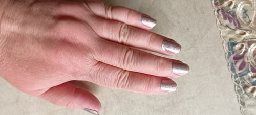 Hand einer Kundin, die die glitzernden UV-Gel-Nagelfolien 'Elegant Glow' auf ihren kurzen, gepflegten Nägeln trägt.