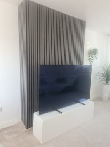 Customer's grey acoustic slatted wall panels installed as a feature wall behind a TV on a white stand.