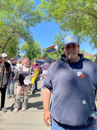 Reviewer wearing a light blue Big Trucker Hat outdoors at a Pride event with a crowd.