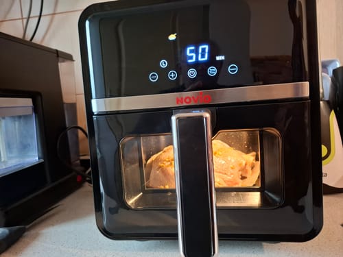 Recenzent gătind un pui întreg în air fryer-ul Novio StonePro. Afișajul digital arată timpul rămas.