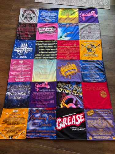 Customer's Project Repat T-Shirt Quilt made from colorful theater and band shirts, laid out fully on a wooden floor.