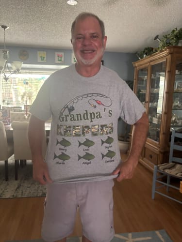 Reviewer smiling while wearing the personalized grey "Grandpa's Keepers" fishing shirt at home.