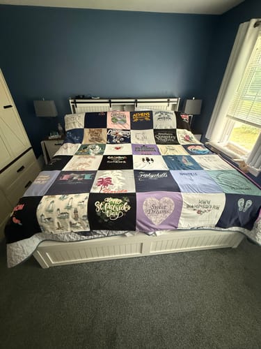 Customer's colorful Project Repat T-Shirt Quilt made from many shirts, neatly displayed on a bed in a bedroom.