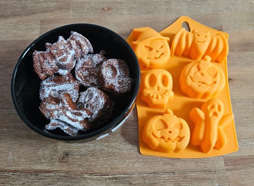 Ein Kunde zeigt die orange Halloween-Silikon-Backform neben einer Schüssel mit dem fertigen, gepuderten Gebäck.