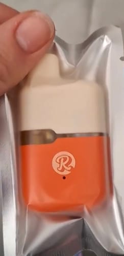 Customer holding the orange and beige 1ML THCA VAPE inside its clear packaging.