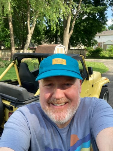Reviewer smiling while wearing their teal Big Camp Hat outdoors.
