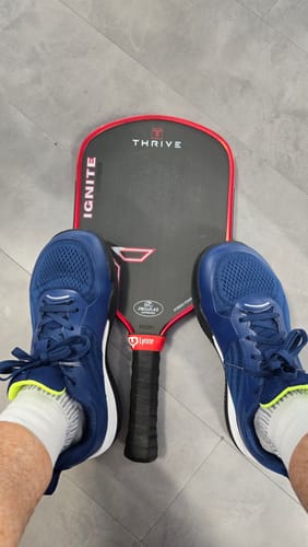 Reviewer's blue CUURT Muuv court shoes shown from above with a pickleball paddle between their feet.