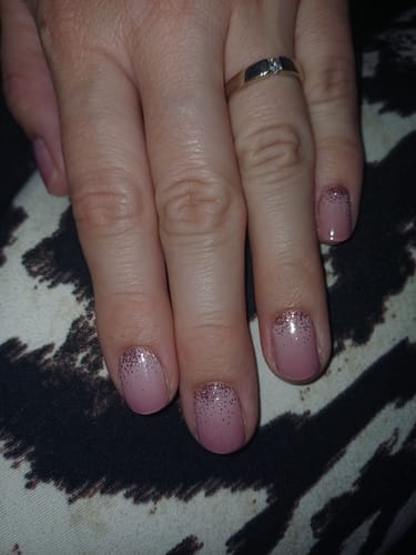 Hand einer Kundin, die die 'Cupcake Sprinkles' UV-Gel-Folien auf kurzen, gepflegten Nägeln mit einem staubrosa Ombré-Glitzer-Design trägt.