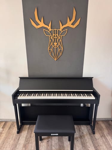 Ein Kunde zeigt sein aufgebautes schwarzes Digitalpiano mit passendem Hocker in einem Raum.