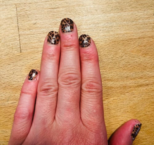 Nahaufnahme der Hand einer Rezensentin, die die 'Cheetah Magic' UV-Nagelfolien mit Tiermuster auf kurzen Nägeln zeigt.