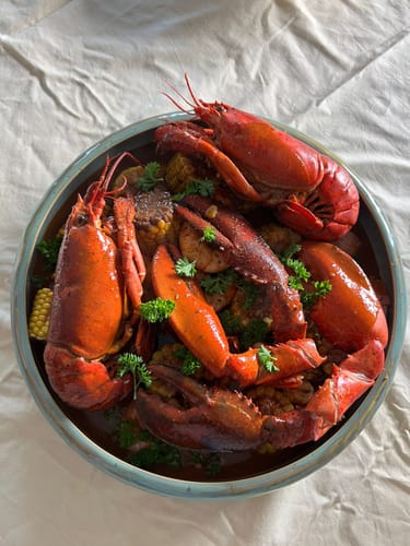 Recensent toont het resultaat van de Cajun Seafood Boil Bomb: een grote schaal met rode kreeften en maïs in saus.