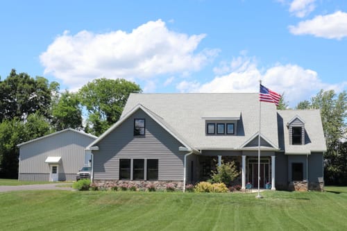 Reviewer's Ultra Heavy-Duty Home Flagpole installed in the front yard of a large, gray house.