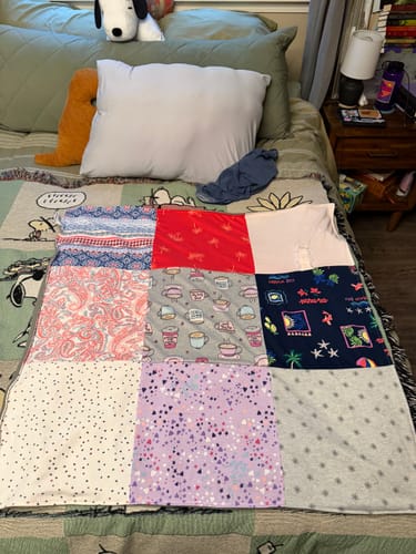Customer's colorful Project Repat T-Shirt Quilt made from sentimental shirts and displayed on a bed.