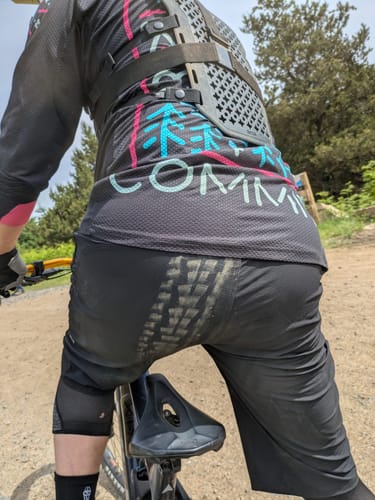 Reviewer on a mountain bike wearing black Spectre Trail Shorts with a muddy tire track across the seat.