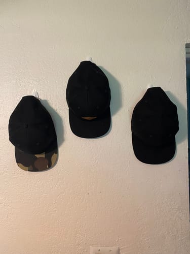 Customer's three hats hanging on a wall, including two black caps and one with a camouflage brim.
