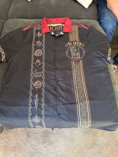 Customer's El Jefe Azteca Guayabera shirt laid flat, showing the detailed front graphics, Aztec patterns, and red collar.