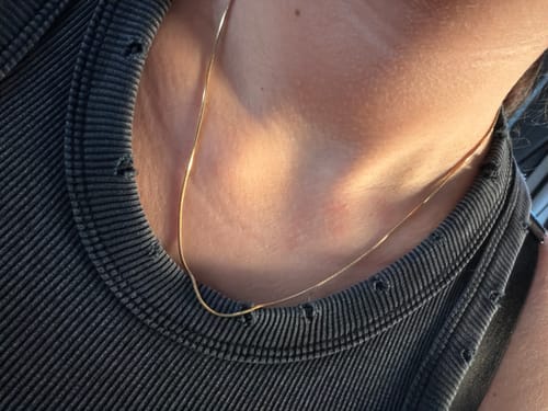 Close-up of a reviewer wearing the thin, gold Carola Necklace against their neck and a dark shirt.