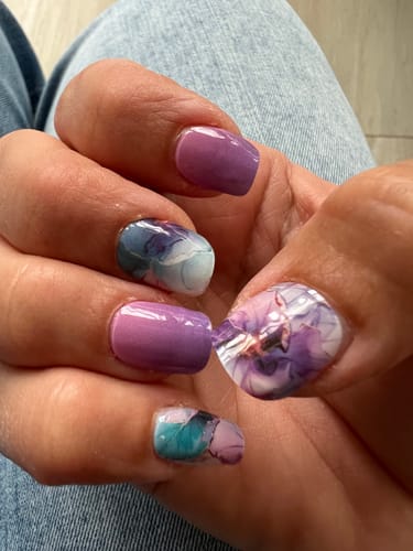 Kundin zeigt ihre Maniküre, die florale und einfarbige 'Pastel Petals' UV-Gel-Folien kombiniert.