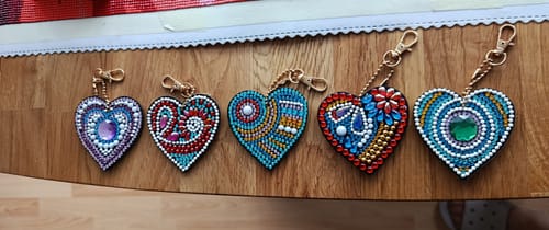 Ein Kunde zeigt die fünf fertig verzierten Herz-Schlüsselanhänger, die auf einem Holztisch liegen.