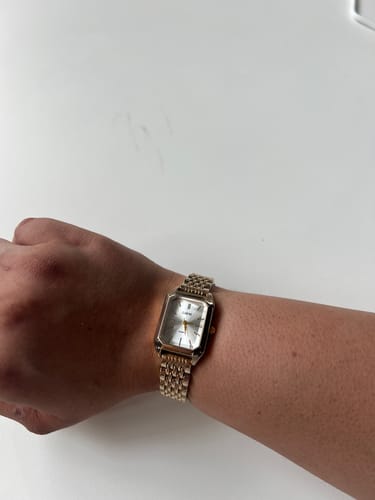 Customer's wrist wearing the gold-colored CLAIRE DE MAINS watch with its classic rectangular face.